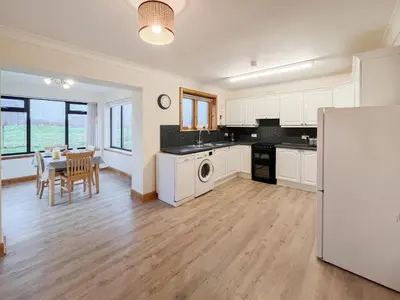 a kitchen with white cabinets and a dining room with a table at Shellhill Cottage in Kirkcudbright
