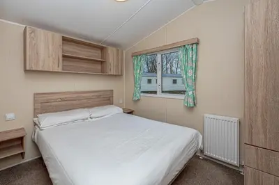 a bedroom with a white bed and a window at Lyons Manor House Caravan Park in Mawbray