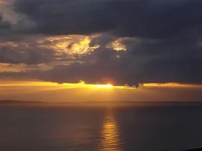 a sunset over the ocean with the sun hiding behind clouds at Airyolland in Newton Stewart