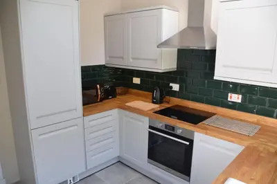 a kitchen with white cabinets and green tiles at Albany Cottage in Rockcliffe