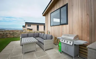 a patio with a grill and a couch and a barbecue at Bluebell Lodge in Girthon