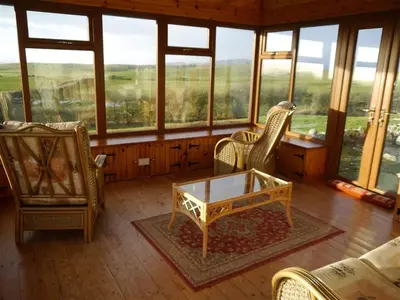 a living room with chairs and a table and windows at Allanhead Cottage in Kirkcudbright