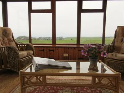 a living room with a table and chairs and windows at Allanhead Cottage in Kirkcudbright