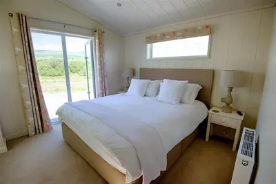 a bedroom with a large bed with a large window at Barley Lodge in Girthon