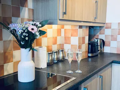 a vase with flowers and wine glasses on a kitchen counter at Pears Suite - 1 Bedroom - Sleeps 2 in Whitehaven