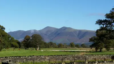 a field with trees and mountains in the background at Lake District, Mountain Views, Accessible Studio Bothy in Borrowdale Valley