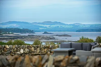 a patio with a stone wall and a couch and a table at Clover Lodge in Gatehouse of Fleet