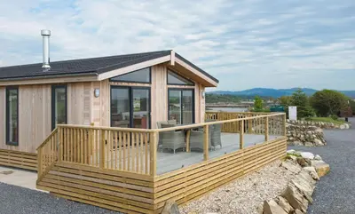 a large wooden cabin with a large deck at Clover Lodge in Gatehouse of Fleet