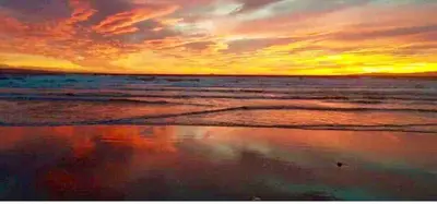 a sunset on the beach with a reflection in the water at Sea Ayr - City Centre Apartment in Ayr