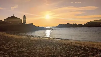 a beach with a lighthouse and the ocean at sunset at Portpatrick 2 bedroom Self Catering Flat in Portpatrick