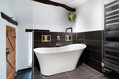 a bathroom with a white tub and black tiles at Bridge End Cottage Elterwater in Ambleside