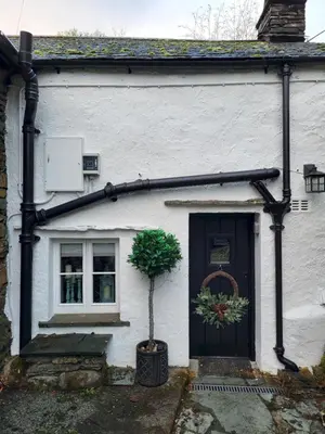 a white house with a black door and a potted plant at Bridge End Cottage Elterwater in Ambleside