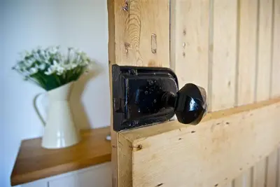 a wooden door with a door knob and a vase of flowers at Meadow Cottage in Girthon