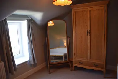 a bedroom with a mirror and a cabinet and a window at Munro Cottage in Rockcliffe