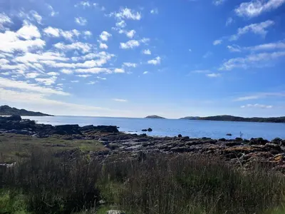 a large body of water with rocks and a cloudy sky at Munro Cottage in Rockcliffe