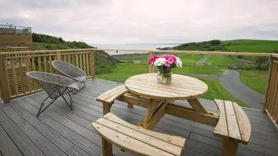 a wooden deck with a table and chairs and a vase of flowers at Pebbles in Girthon