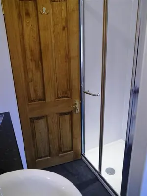 a bathroom with a shower and a wooden door at Primrose Cottage in Rockcliffe