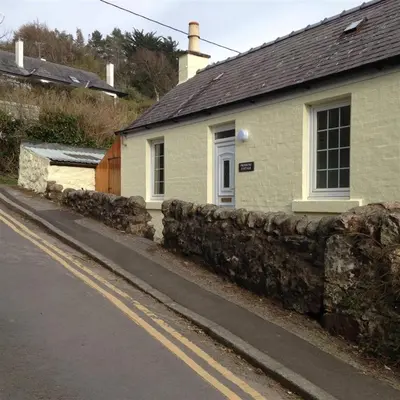 a white house with a stone wall next to a street at Primrose Cottage in Rockcliffe