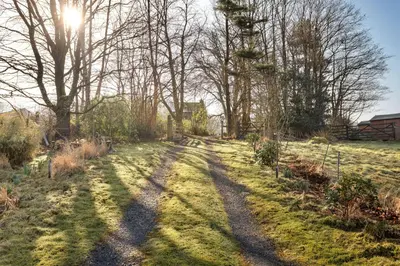 a path in a field with the sun shining through trees at Finest Retreats - St Francis Cottage in Ulpha