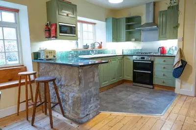 a kitchen with green cabinets and a stone island at Gardeners Cottage in Auchencairn