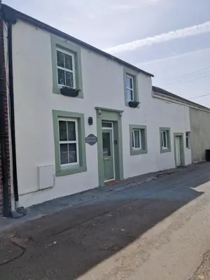 a white house with green windows and a street at Victoria Cottage in Whitrigg