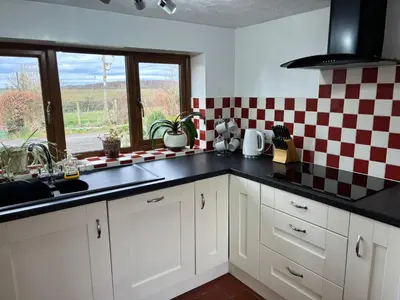 a kitchen with white cabinets and a checkered wall at Kingate Cottage in Aspatria