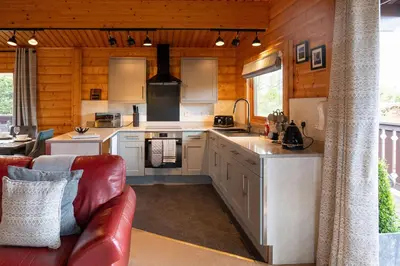 a kitchen with white cabinets and a red leather couch at Ravens Craig in Kippford