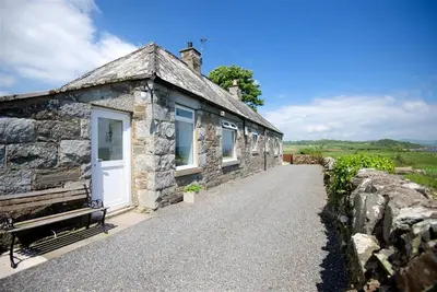 a stone cottage with a white door and a stone wall at Threaby Cottage in Girthon