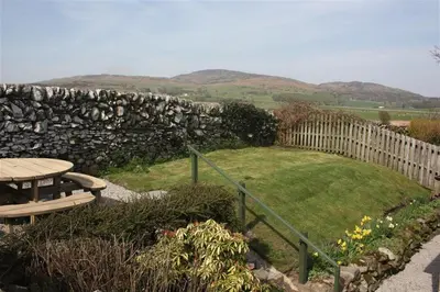 a stone wall and a picnic table in a garden at Threaby Cottage in Girthon