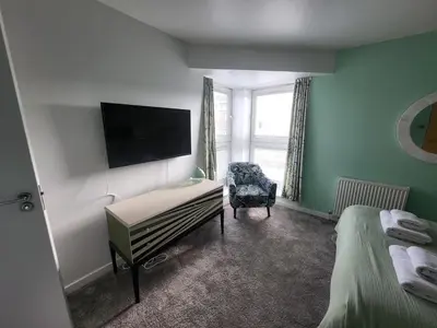a room with two beds and a chair and a television at River Ayr View-Coorie Doon Stays in Ayr