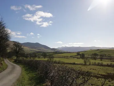 a road in a field with mountains in the background at Longlands Lodge in Wigton
