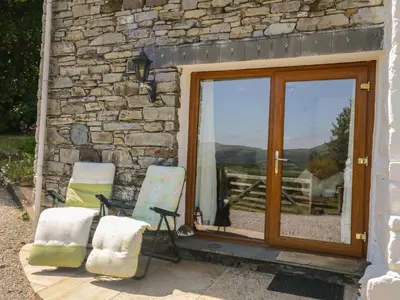 two chairs sitting next to a stone building with a door at Wren's Nest in Keswick