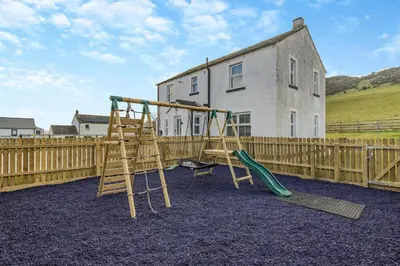 a playground with two swings and a wooden fence at 3 Bed in Cockermouth oc-o31515 in Embleton