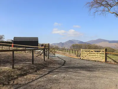 a fence on a dirt road with mountains in the background at Shepherds View in Keswick