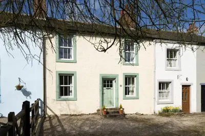 a white house with green windows and a fence at Riverside - Quaint County Cottage overlooking the Beck in Caldbeck