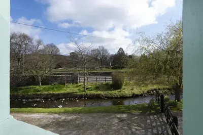 a view of a river with a bench and a fence at Riverside - Quaint County Cottage overlooking the Beck in Caldbeck