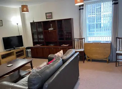 a living room with a leather couch and a television at 3 Telford Mews in Dumfries