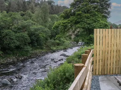a wooden fence next to a river with trees at Sail Luxury Family Pod in Keswick