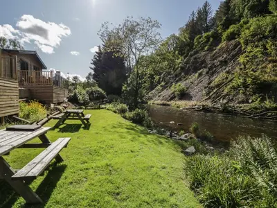 a picnic table in the grass next to a river at Elter Luxury Pod in Keswick