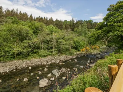 a river with rocks and trees in the background at Woof Luxury Family Pod in Keswick