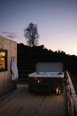 a hot tub sitting on a deck with candles at The Byre, Summerhill Farm Stays in Balmaclellan