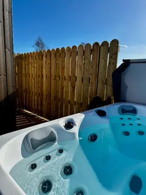 a hot tub in front of a wooden fence at The Barn, Summerhill Farm Stays in Balmaclellan