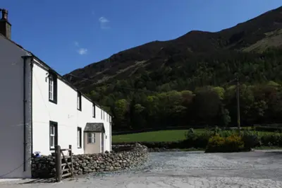 a white building with a stone wall next to a mountain at Sandhills Farm in Bassenthwaite