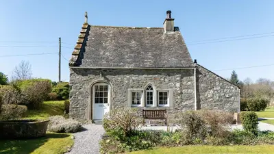 an old stone cottage with a bench in a garden at Cross Cottage in Gatehouse of Fleet