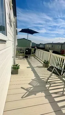 a wooden deck with chairs and an umbrella at Shoreline Stay in Port Carlisle