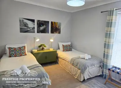 a bedroom with two beds and a desk and a window at Harcourt by Prestige Properties SA in Workington