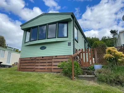 a green tiny house with a wooden fence at Grannys Vintage Coastal Caravan in Kippford