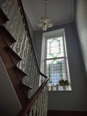 a staircase with a chandelier and a stained glass window at 95 St Mary Street in Kirkcudbright