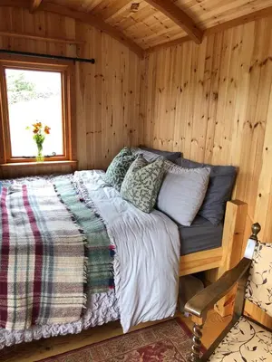 a bed in a wooden room with a window at Barmoffity Shepherds Hut in Kirkpatrick Durham