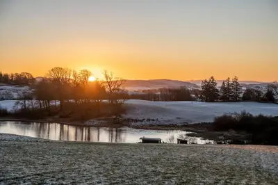a winter sunset in a field with a pond at Barmoffity Shepherds Hut in Kirkpatrick Durham